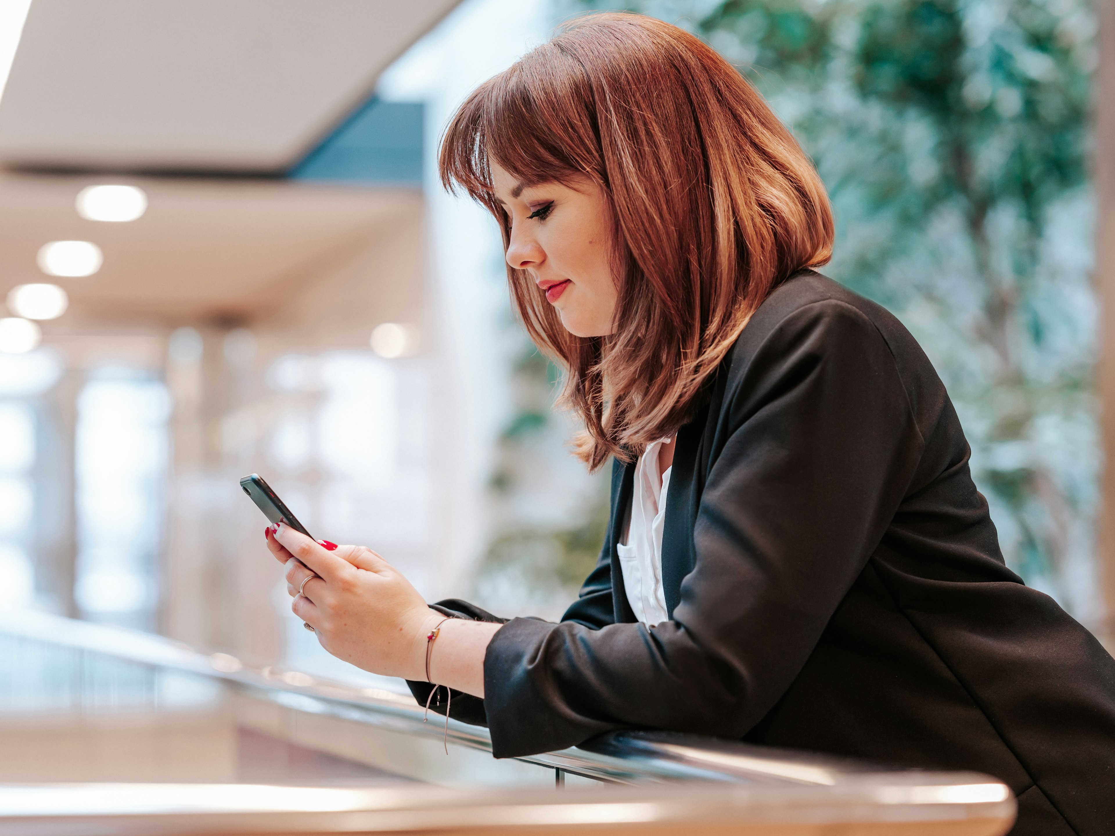 Businessfrau mit Smartphone in der Hand, vertieft in eine Nachricht oder Information, aufgenommen in einer hellen und modernen Büroumgebung.