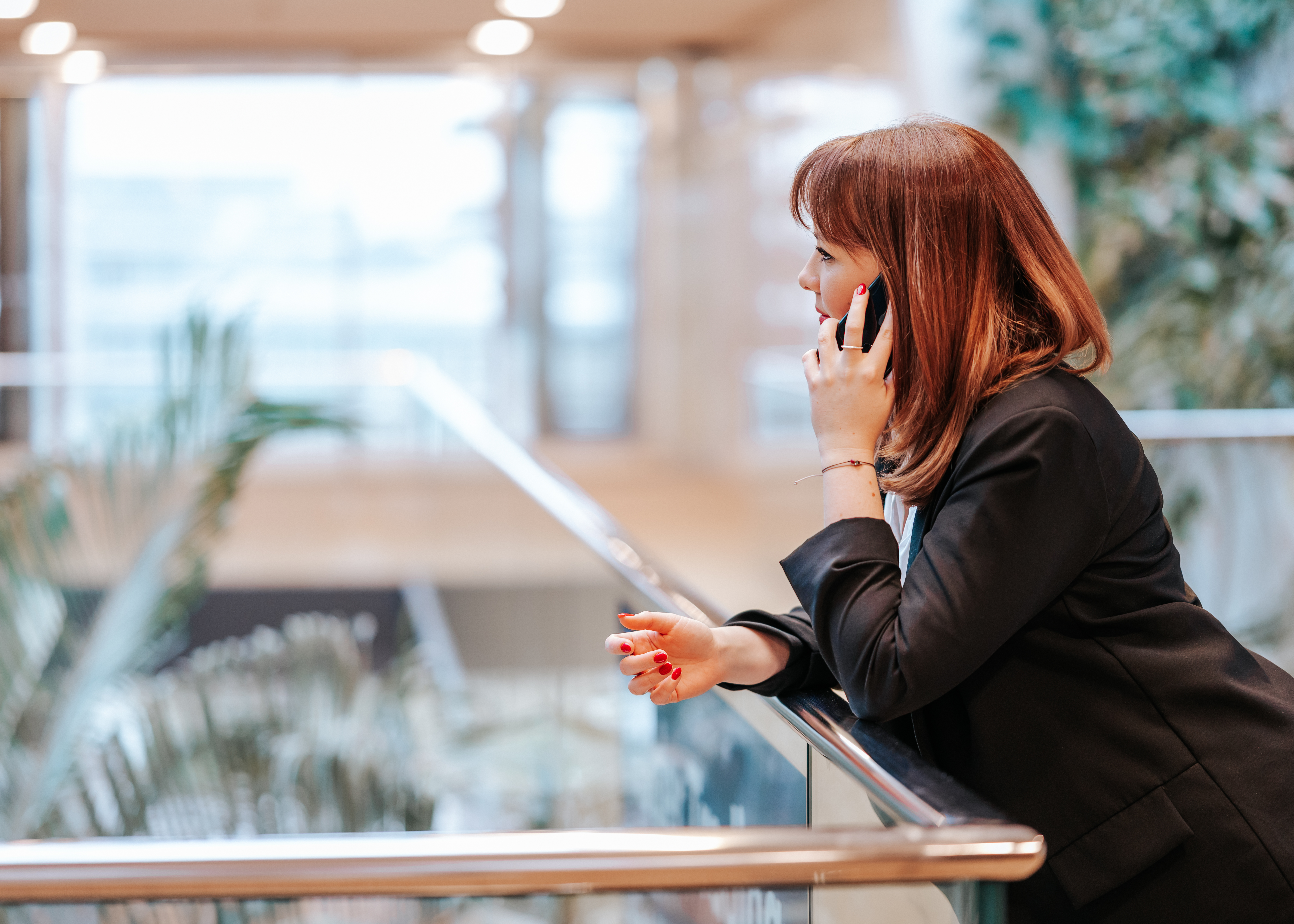 Mitarbeiterin der Baaderbank im schwarzen Blazer telefoniert mit dem Smartphone im modernen Bürogebäude.