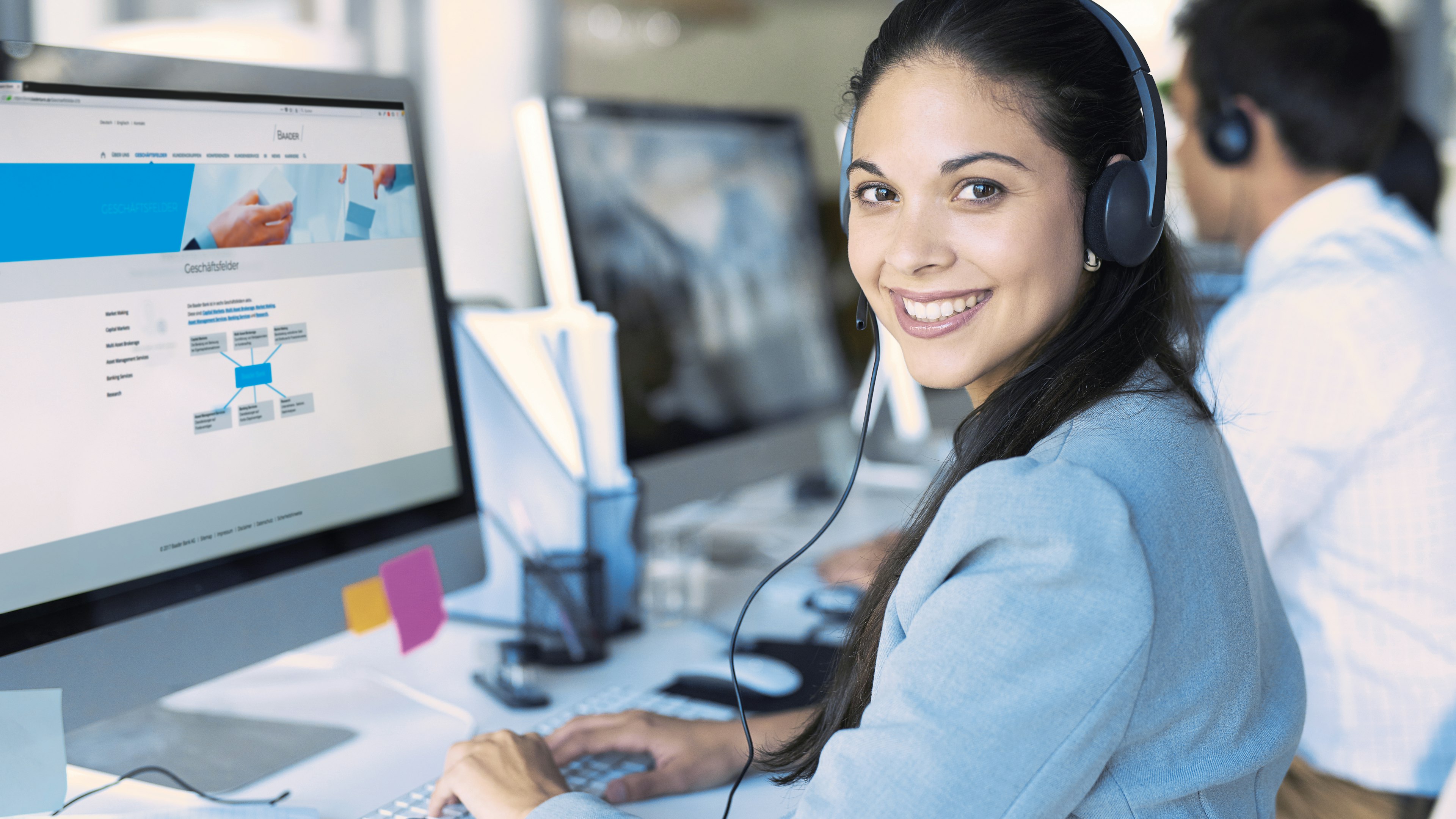 Freundliche Baaderbank Mitarbeiterin im Kundenservice mit Headset am Computer.