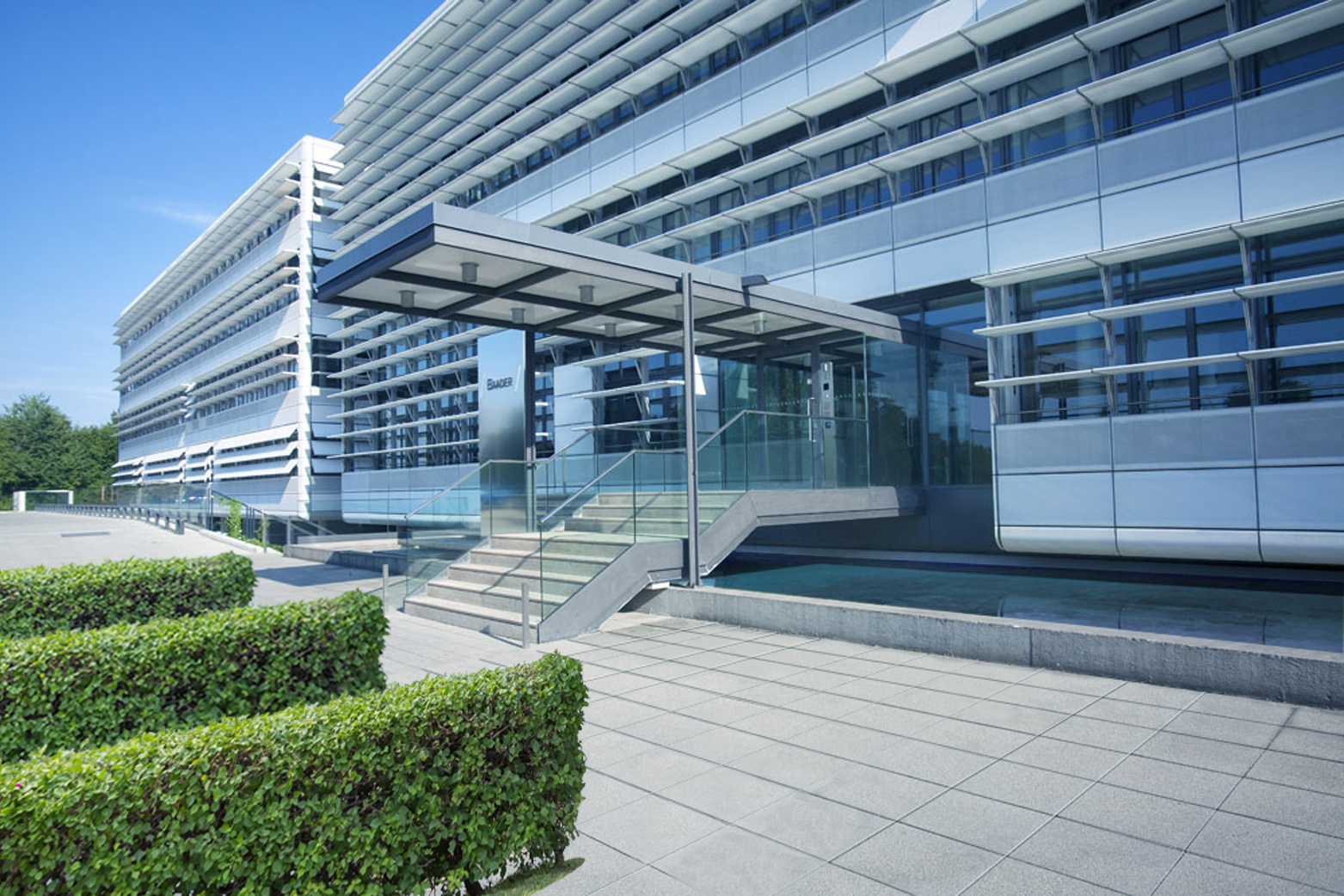 Moderner Eingangsbereich der Baader Bank Zentrale mit Glasfassade, breiter Treppe und klaren architektonischen Linien bei sonnigem Wetter.