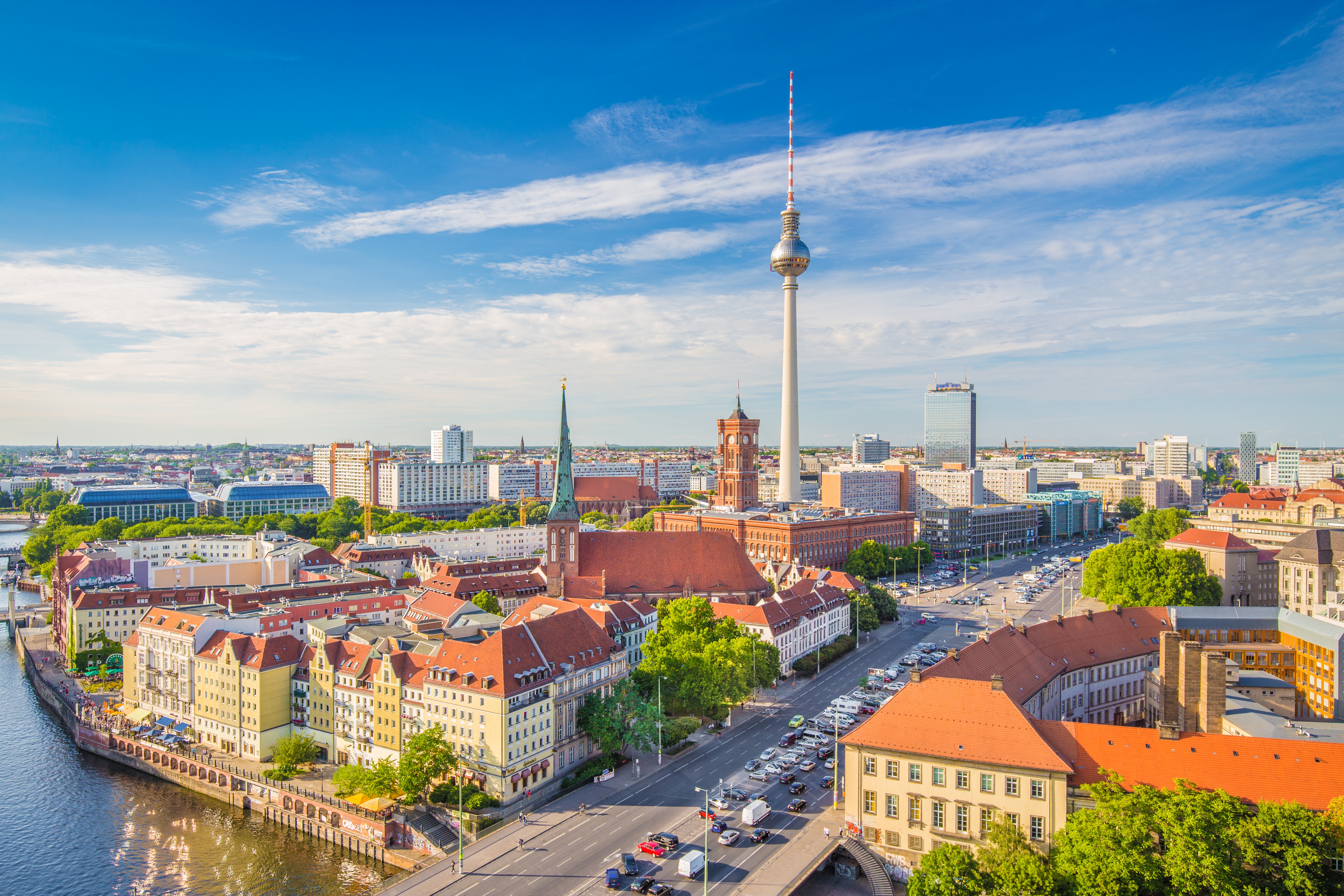 Stadtansicht von Berlin mit Fernsehturm, Rotem Rathaus und weiteren markanten Gebäuden im Sonnenschein, im Vordergrund Häuser mit roten Dächern an der Spree.