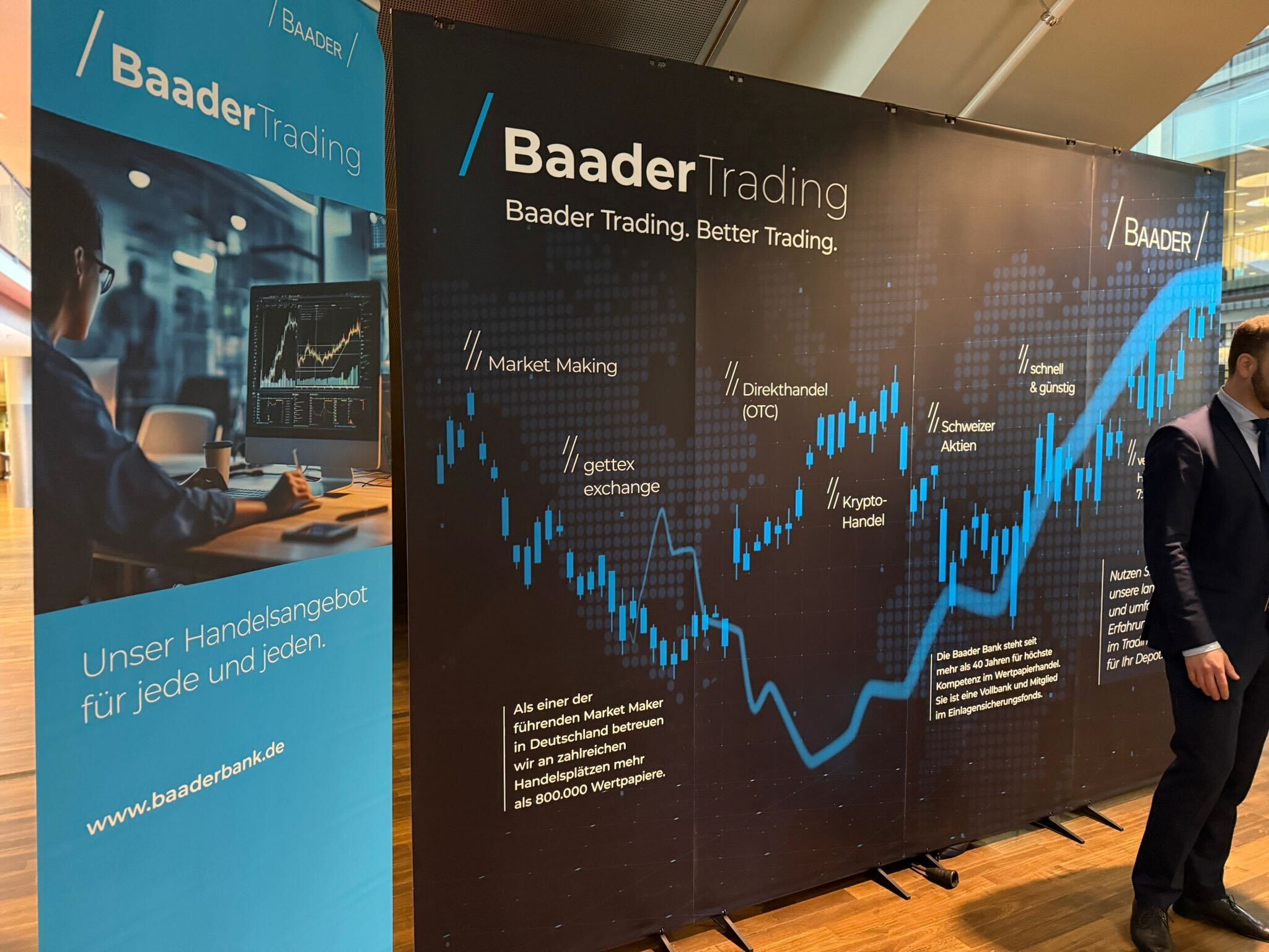 Baader Bank Messestand mit Infowänden zu Baader Trading und Handelsangeboten, dekoriert in Blau und Schwarz, mit Texten und Grafiken zu Trading-Dienstleistungen.