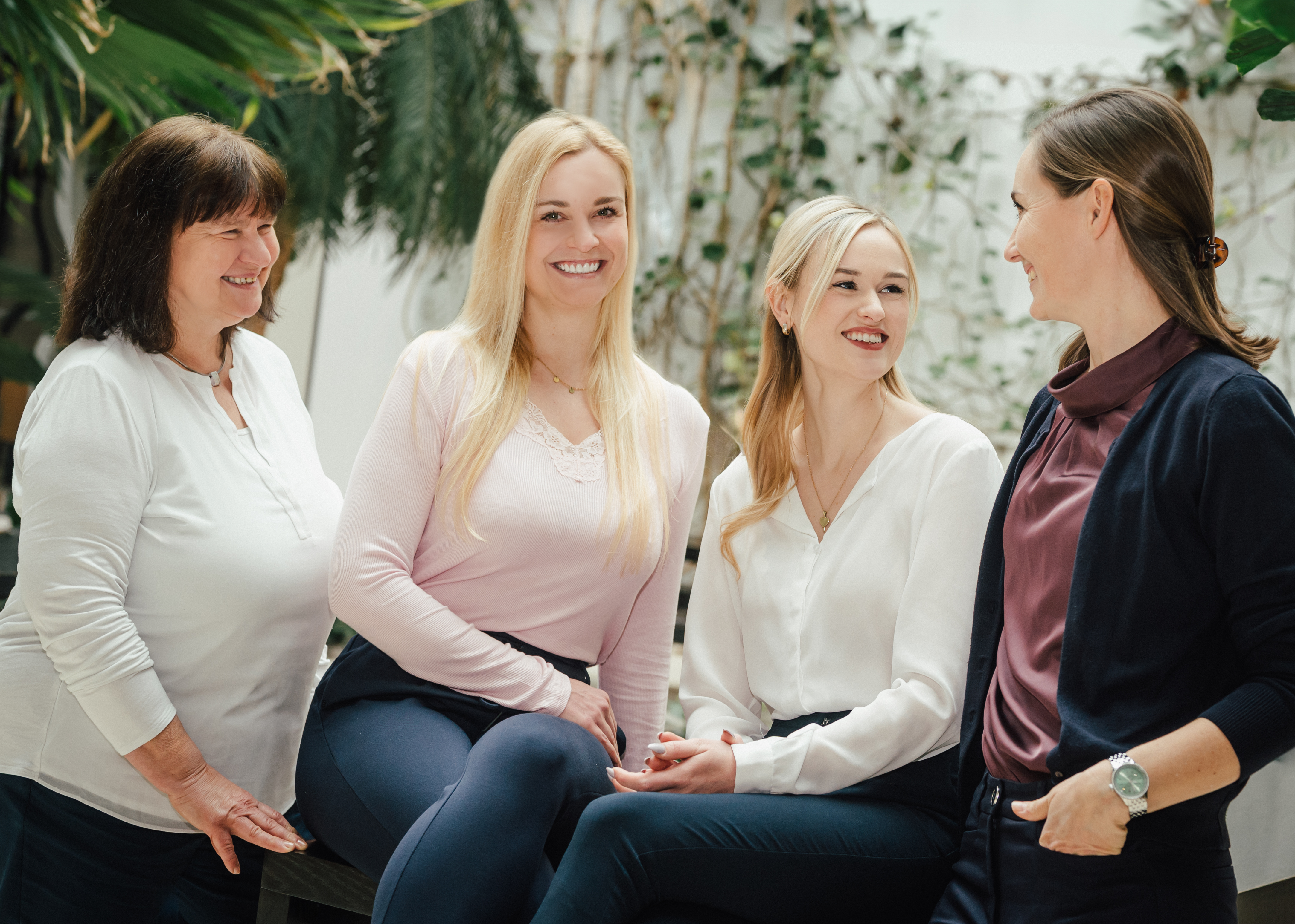 Vier Frauen sitzen und stehen nebeneinander, lächeln in Richtung Kamera.