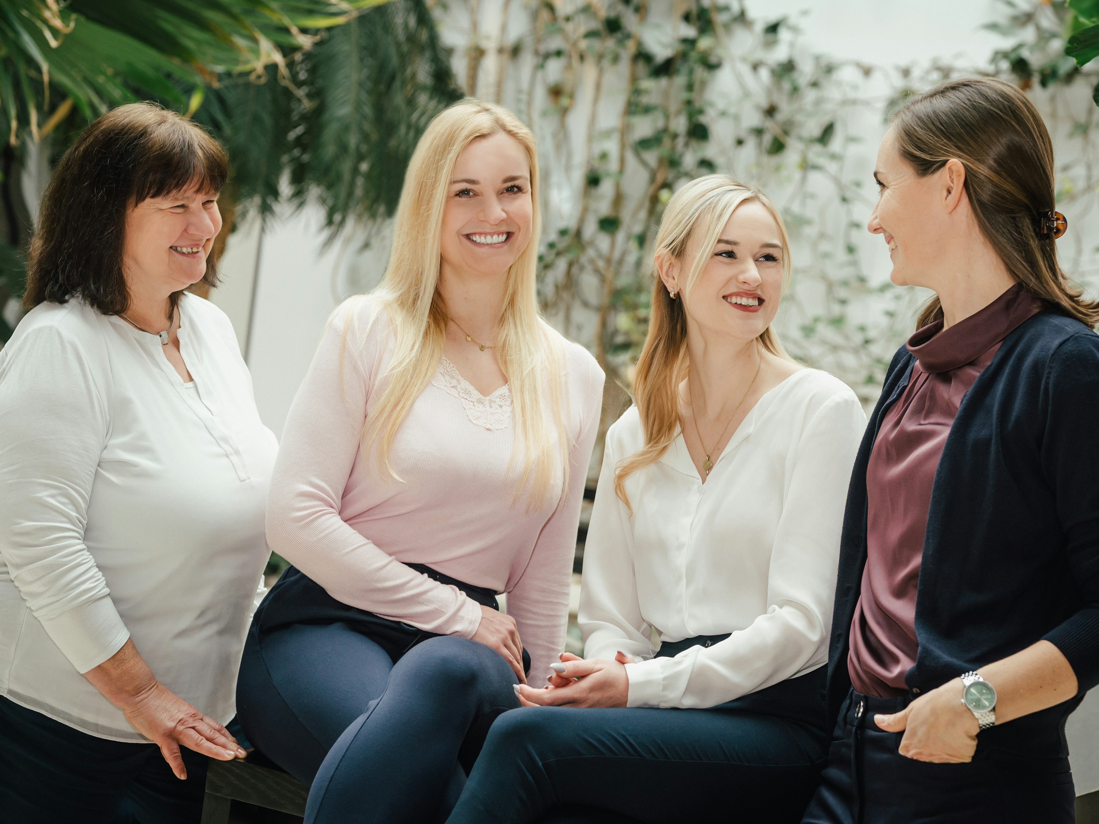 Vier Frauen sitzen und stehen nebeneinander, lächeln in Richtung Kamera.