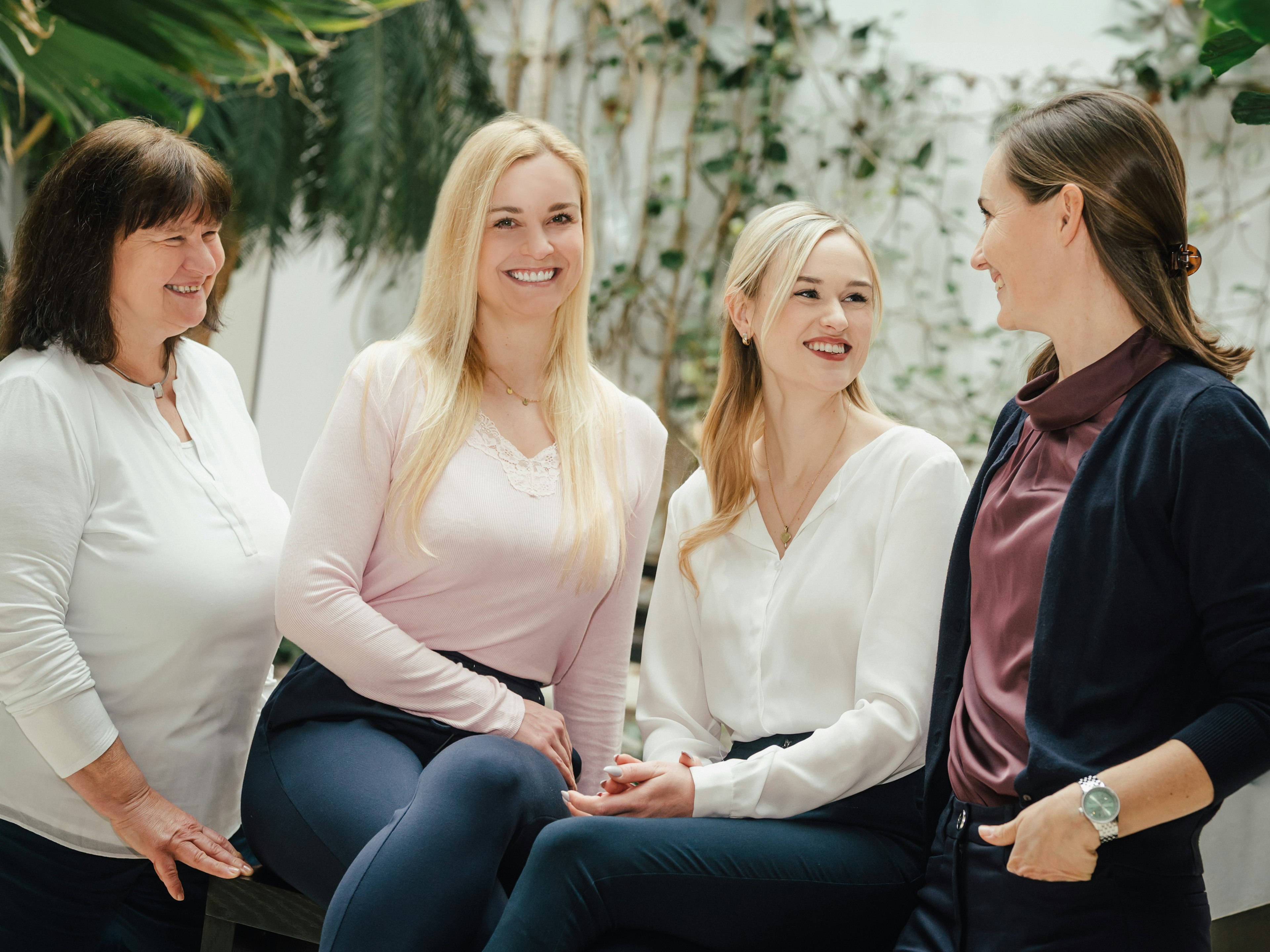 Vier Frauen sitzen und stehen nebeneinander, lächeln in Richtung Kamera.