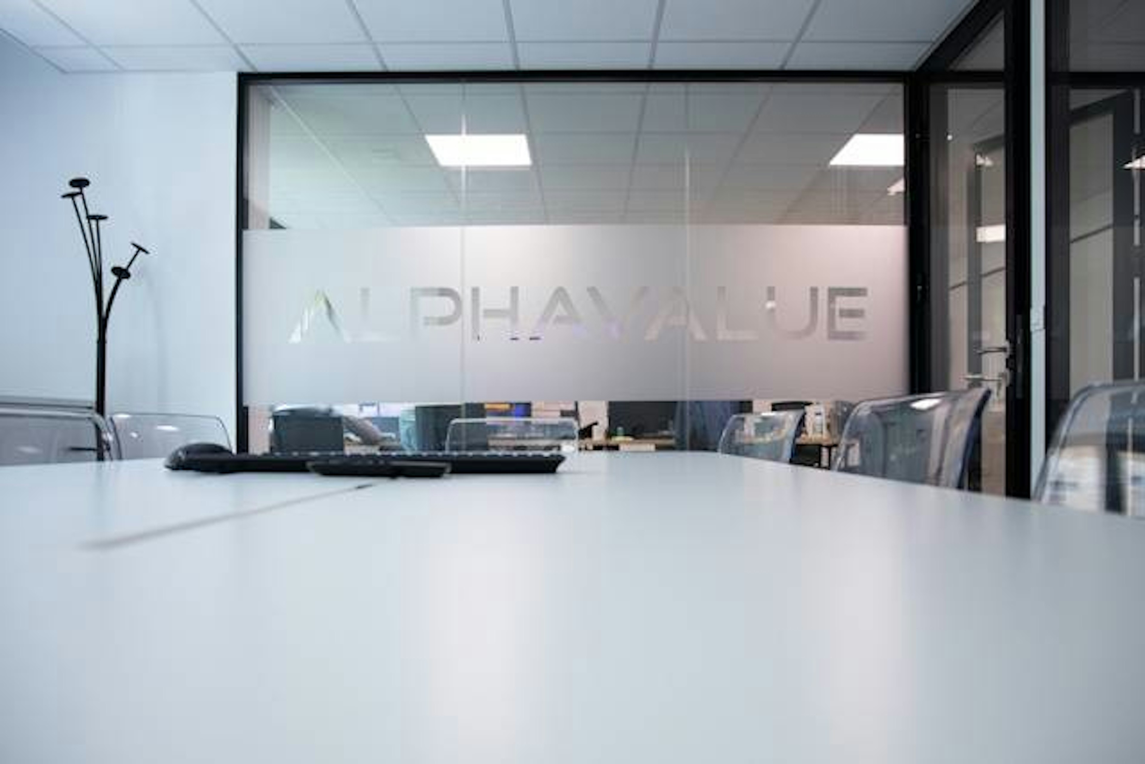 Konferenzraum mit Glaswand und Schriftzug Alphavalue, Blick auf Bürostühle und Tisch.