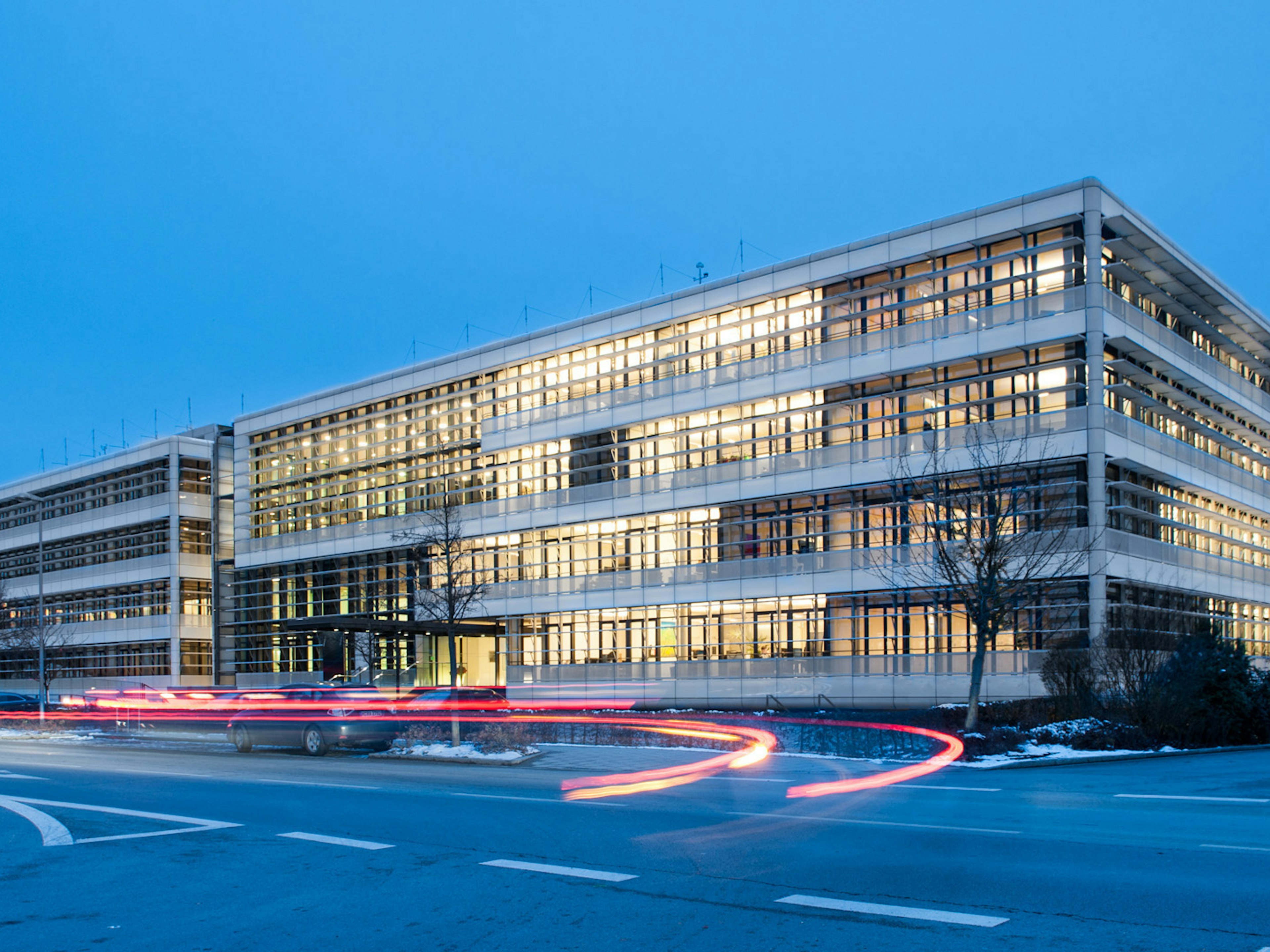 Modernes Bürogebäude der Baaderbank in Unterschleißheim mit beleuchteten Fenstern am Abend.