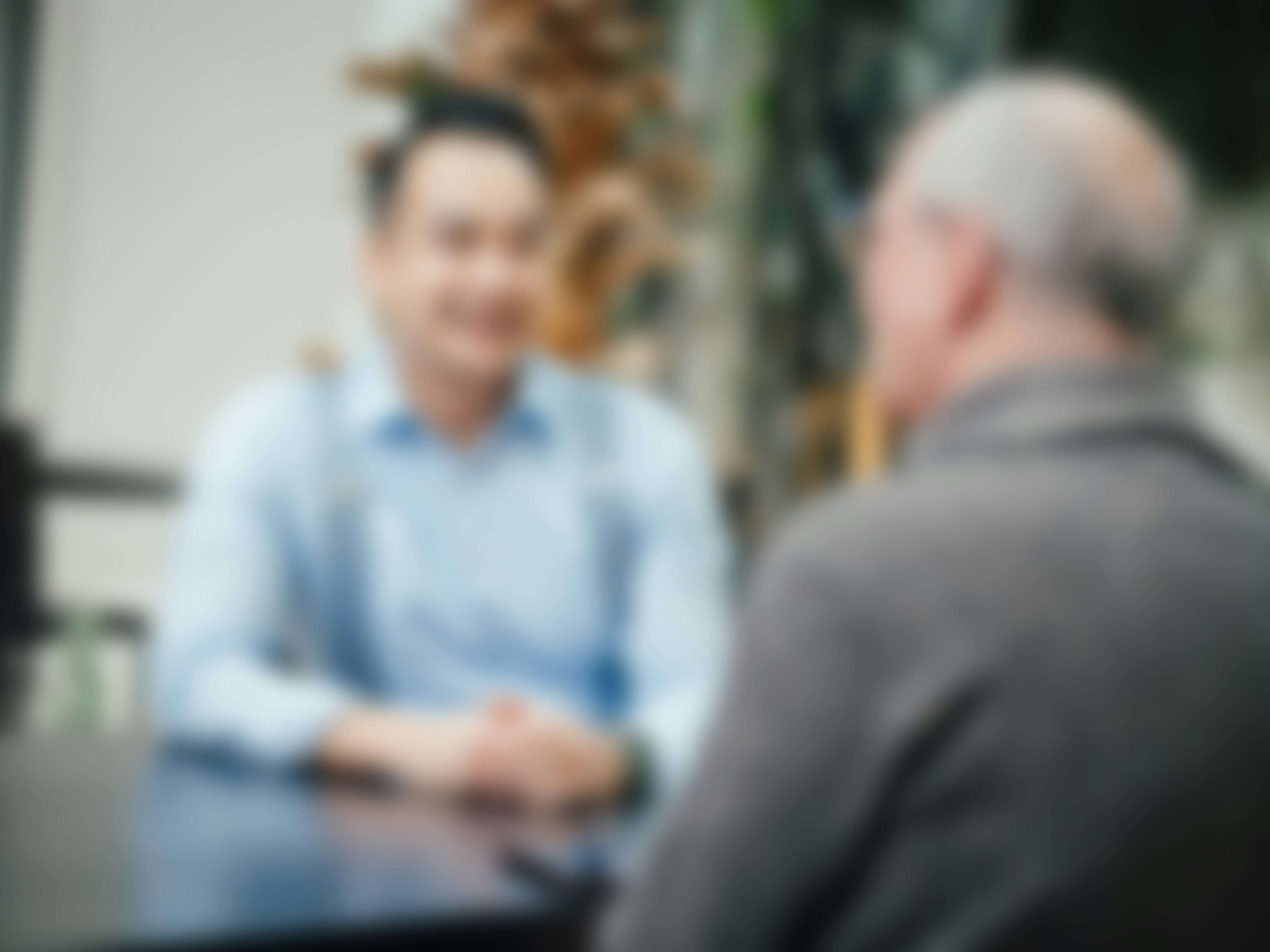 Verschwommene Aufnahme von zwei Personen im Gespräch in einer modernen Umgebung.