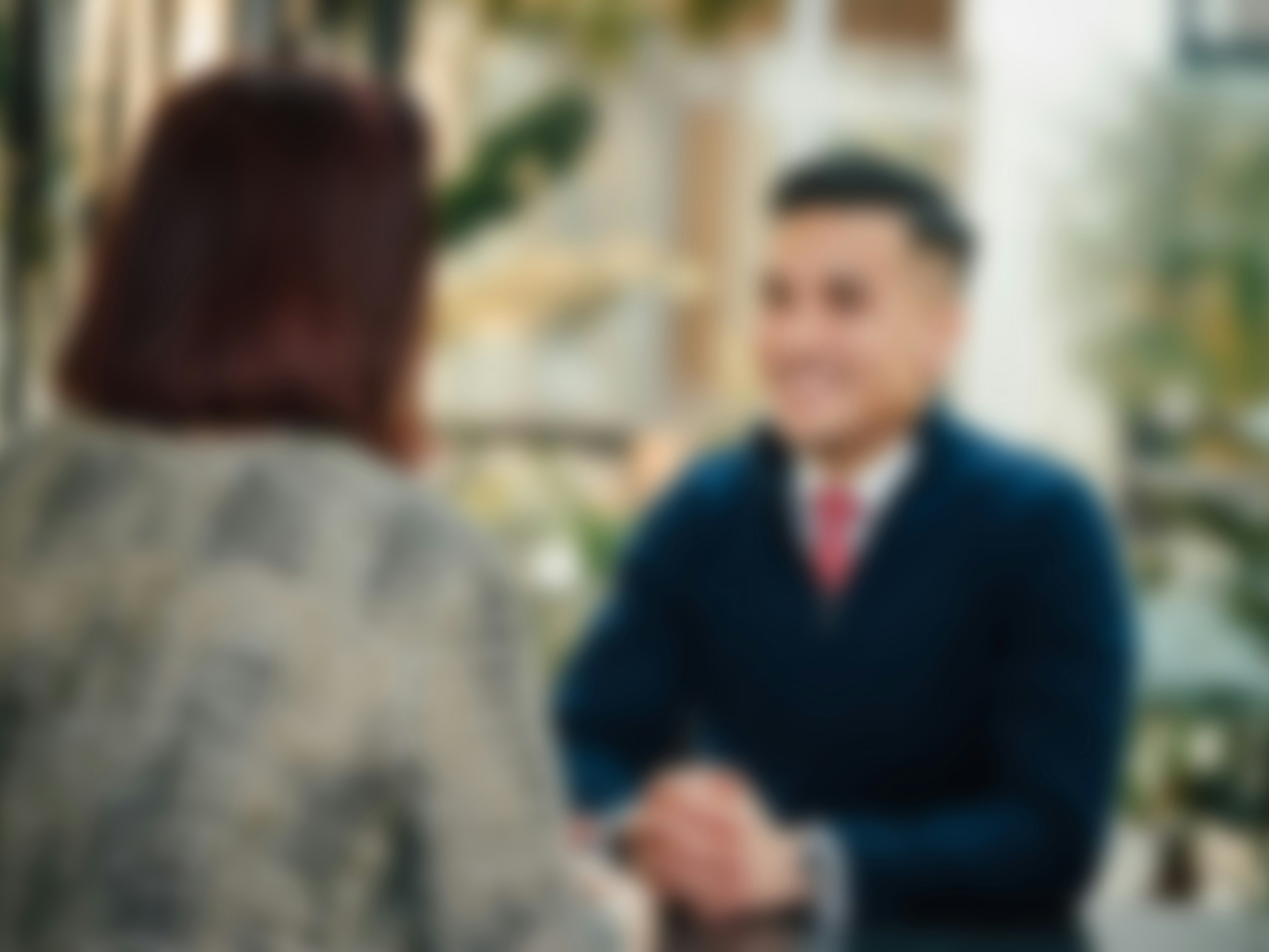 Verschwommenes Bild von zwei Personen im Gespräch, eine frontal, die andere von hinten sichtbar.