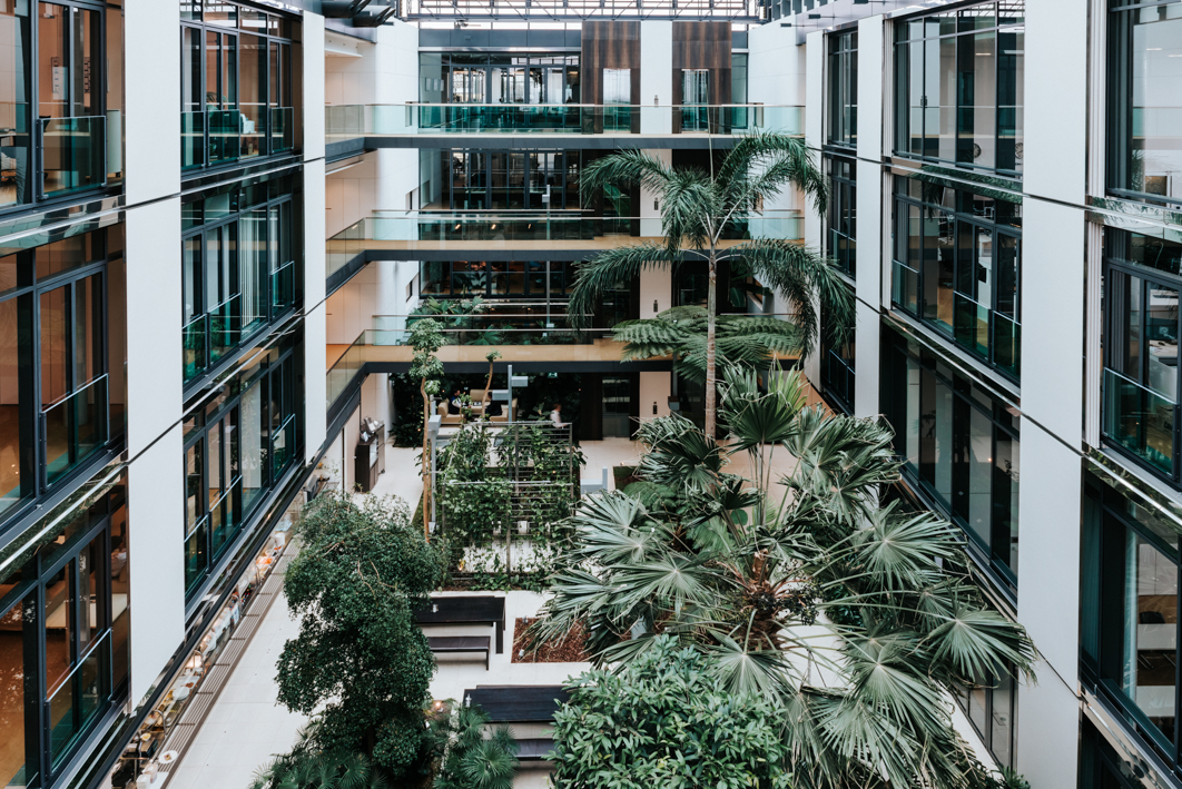 Baaderbank Atrium in Unterschleißheim mit moderner Glasfassade, tropischen Pflanzen und offenen Arbeitsbereichen.