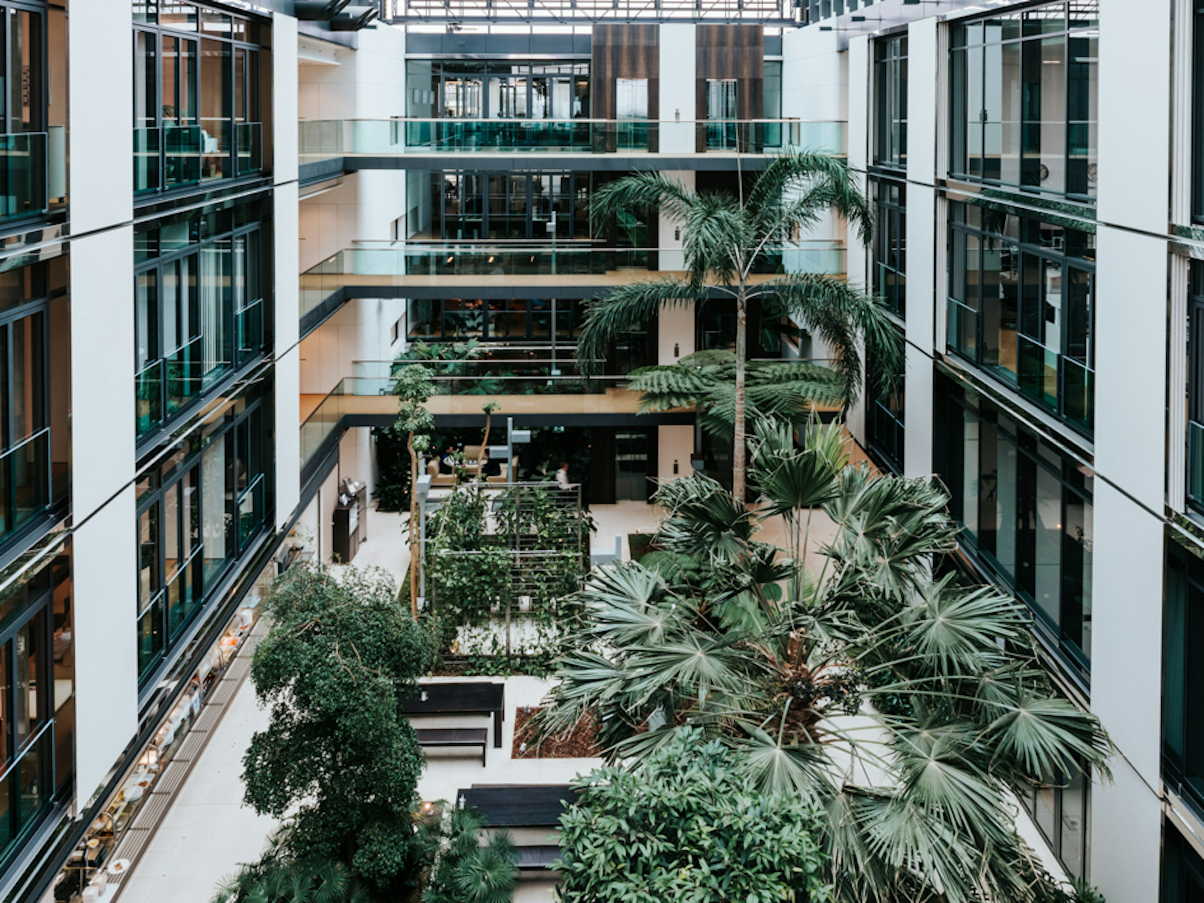Baaderbank Atrium in Unterschleißheim mit moderner Glasfassade, tropischen Pflanzen und offenen Arbeitsbereichen.