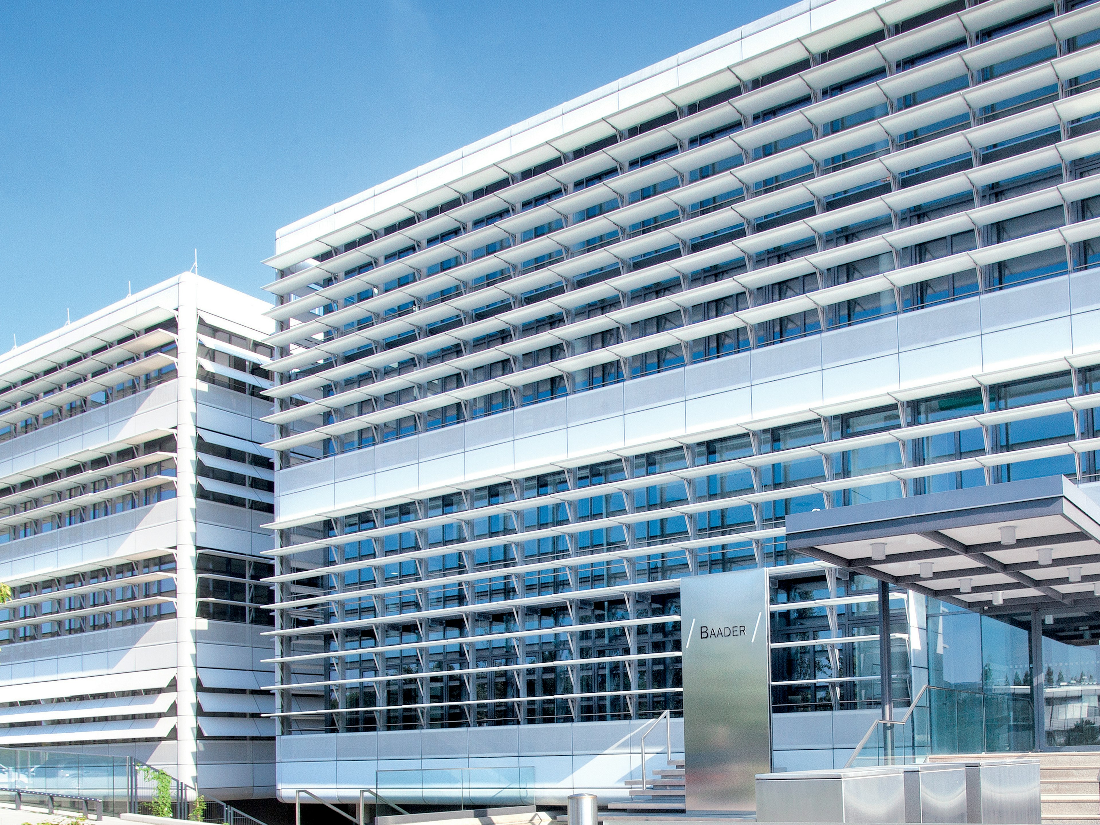 Moderne Baaderbank Zentrale in Unterschleißheim mit Glasfassade, Eingang und Baum im Vordergrund.