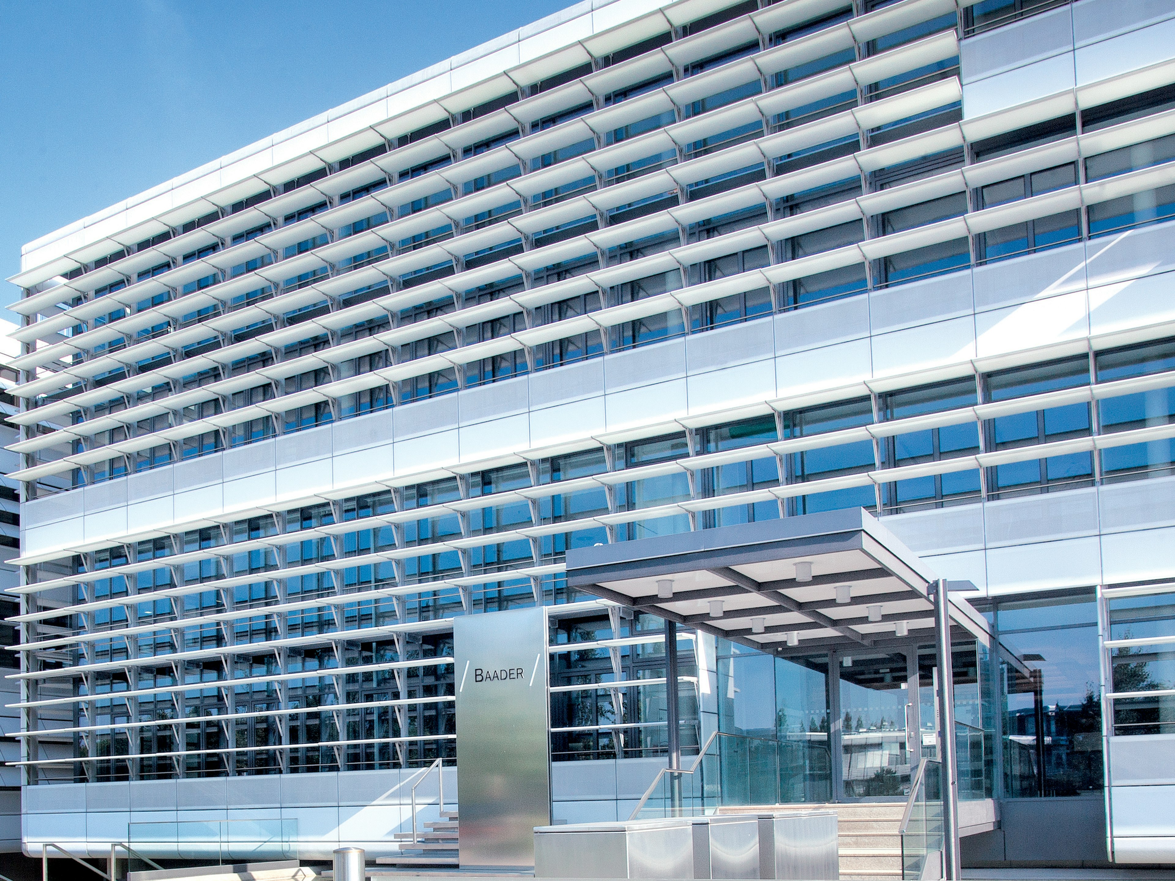 Moderne Baaderbank Zentrale in Unterschleißheim mit Glasfassade, Eingang und Baum im Vordergrund.