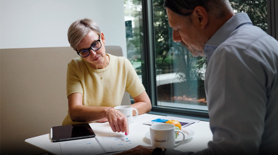Zwei Personen sitzen an einem Tisch, besprechen Dokumente und trinken Kaffee.