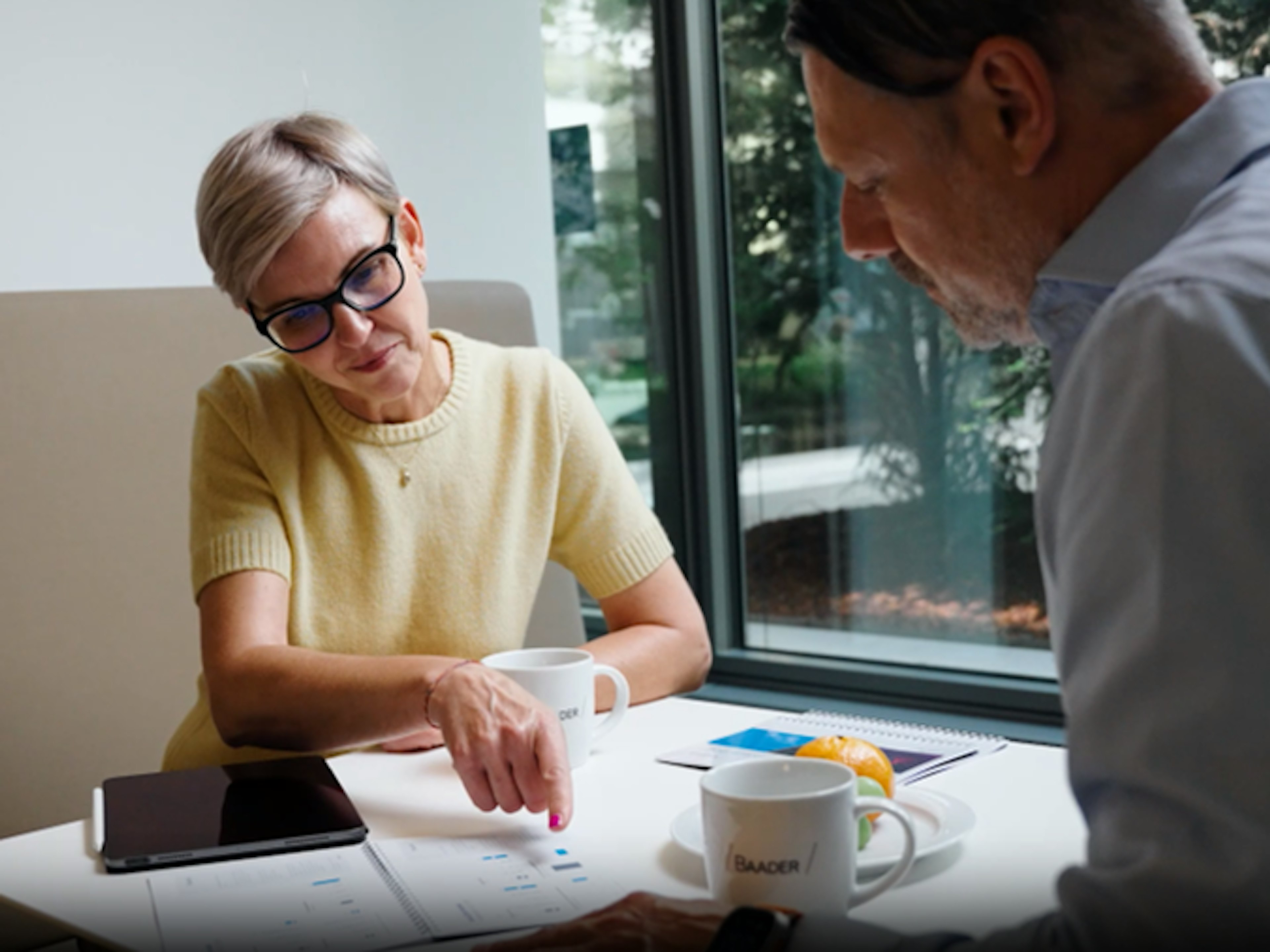 Zwei Personen sitzen an einem Tisch, besprechen Dokumente und trinken Kaffee.