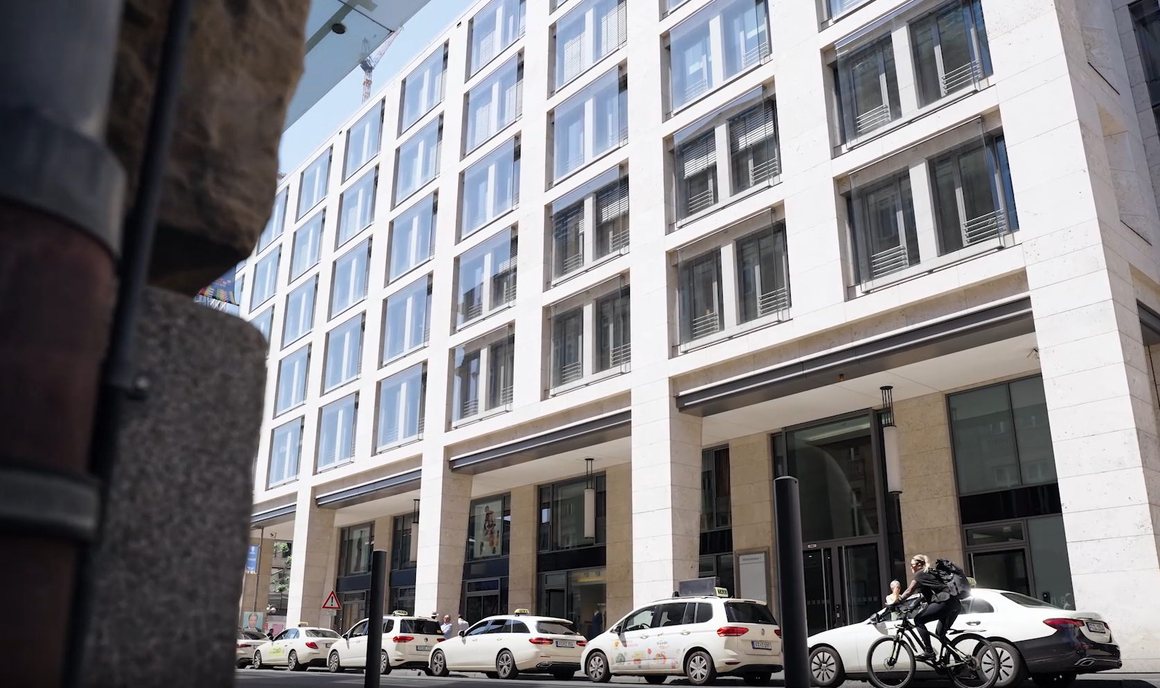 Moderner Standort der Baaderbank mit großer Fensterfassade, davor parkende Taxis und ein Radfahrer.