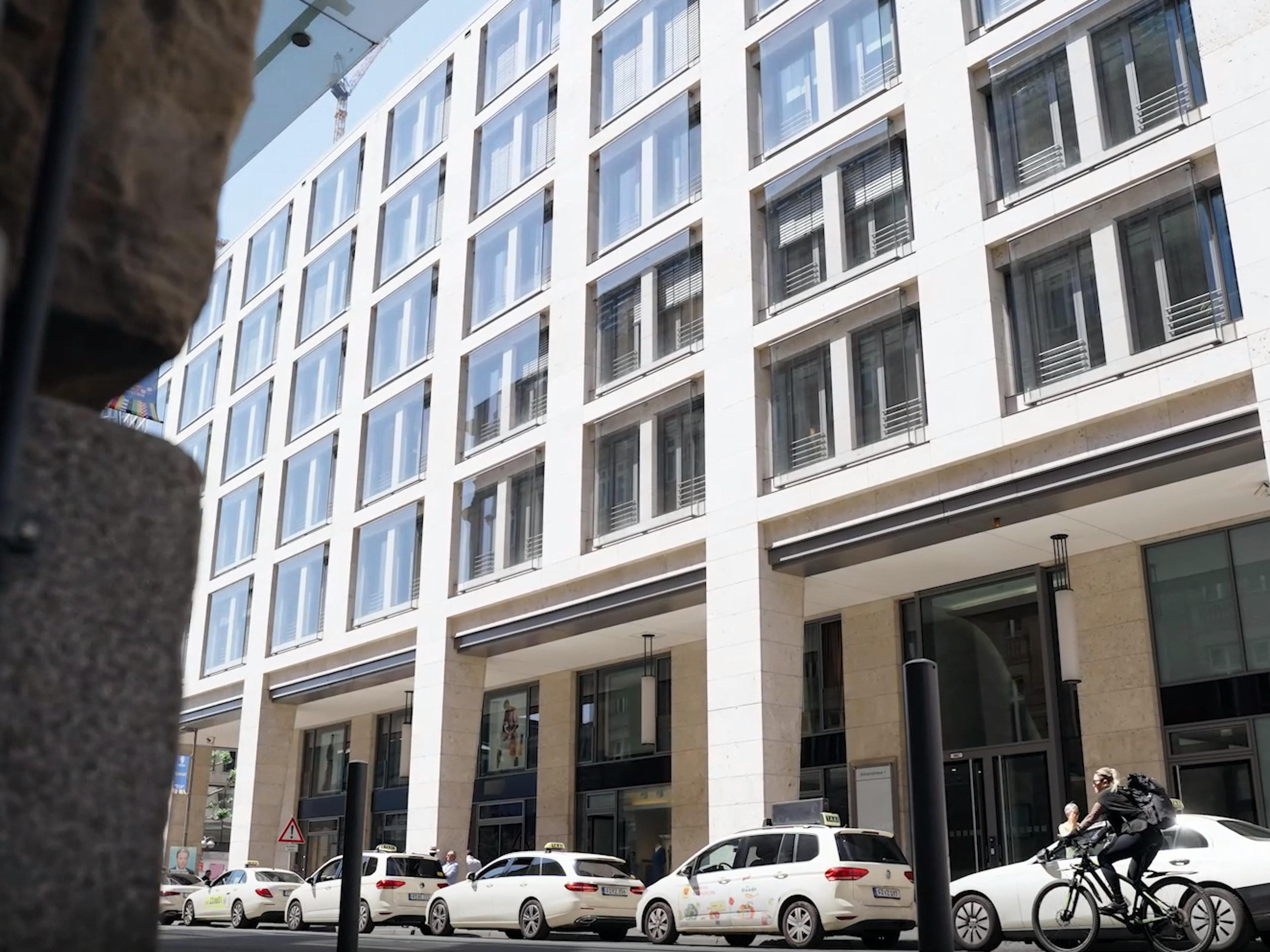 Moderner Standort der Baaderbank mit großer Fensterfassade, davor parkende Taxis und ein Radfahrer.