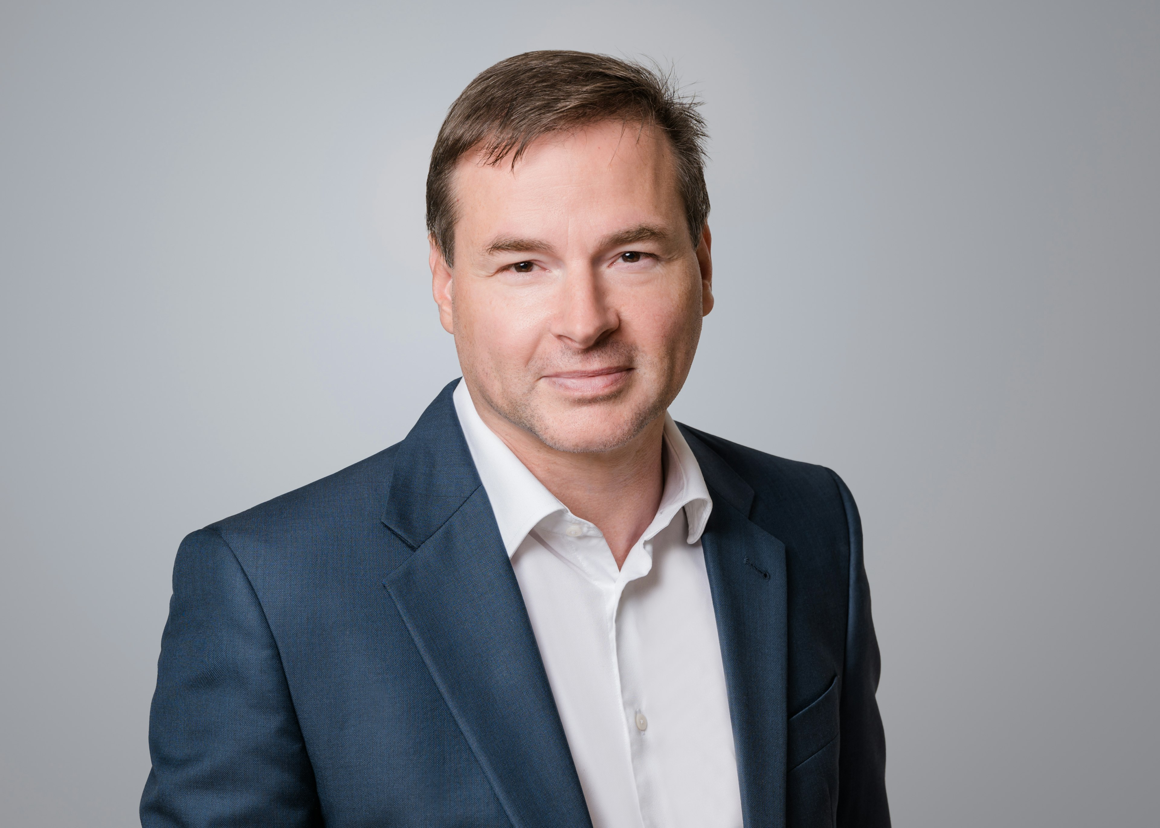 Porträt eines Mannes im blauen Anzug vor grauem Hintergrund.