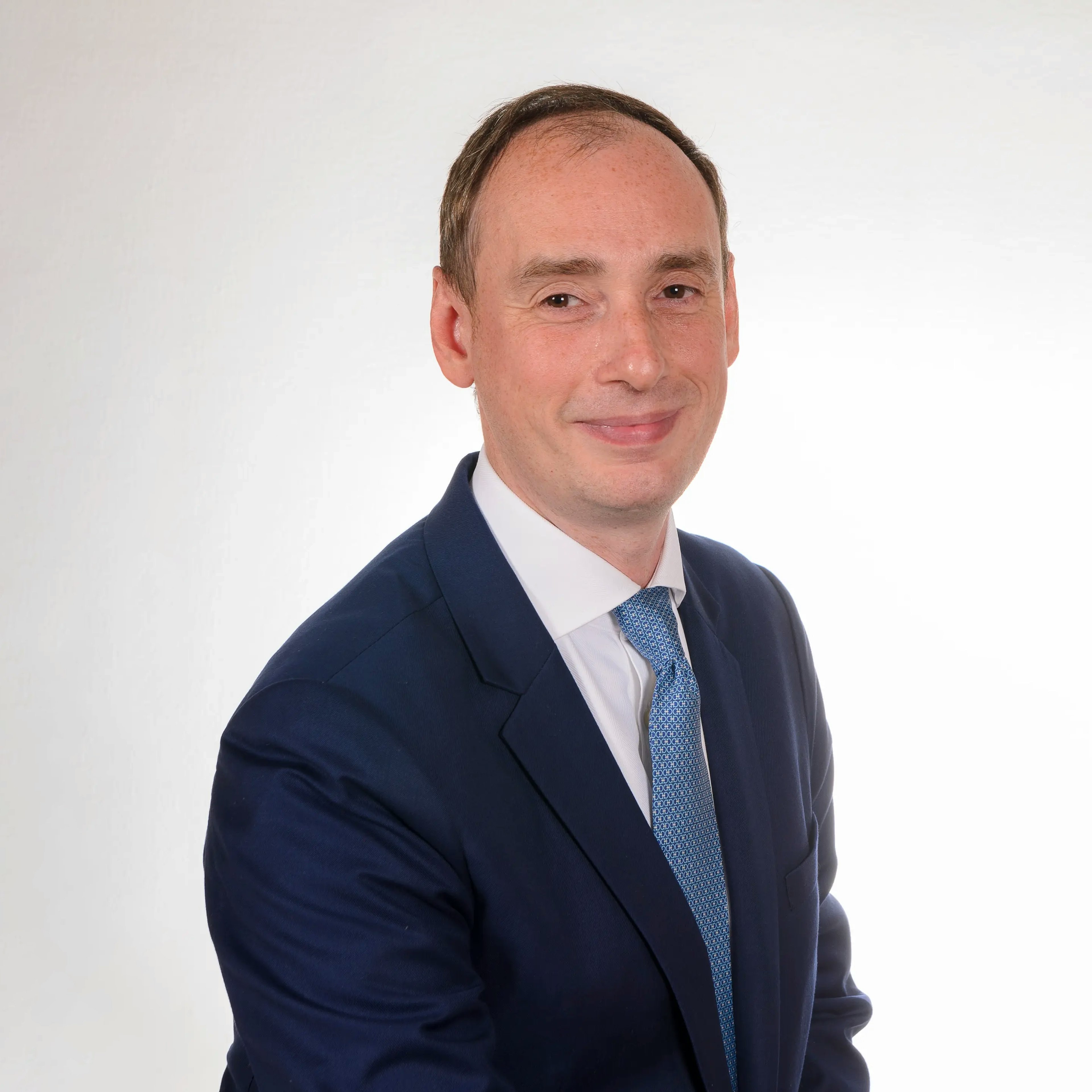 Porträt eines Mannes im blauen Anzug mit Krawatte vor hellem Hintergrund.