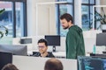 Zwei Entwickler in einem modernen Büro, einer sitzend vor dem Monitor, der andere stehend daneben und zuschauend.