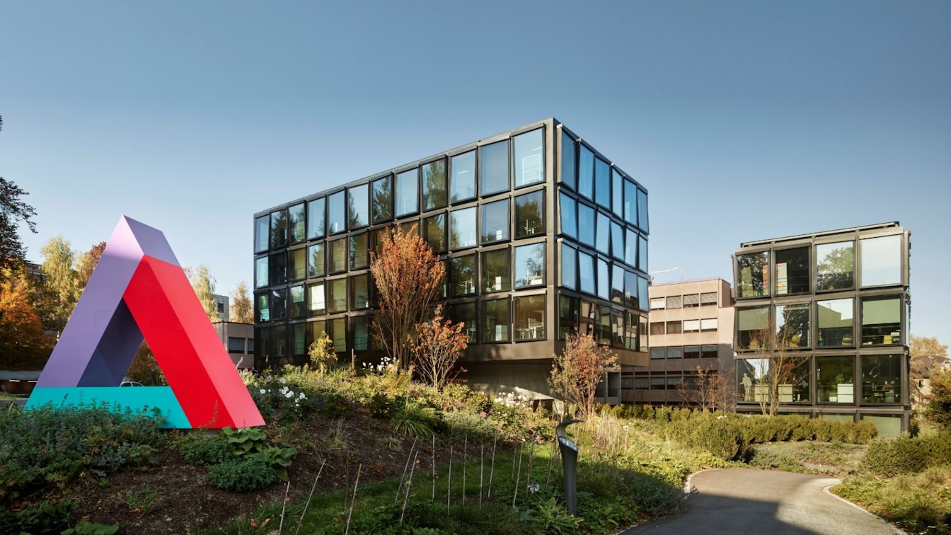 Ein Gebäude der Helvetia Versicherung, fotografiert von aussen mit einer grossen Skulptur im Vordergrund in der Form des Logos der Helvetia Versicherung.