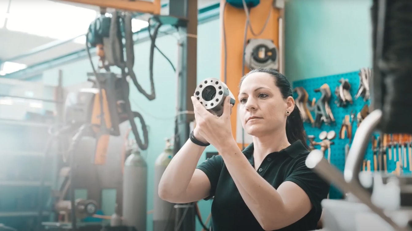 Eine Mitarbeiterin von Spühl in der Werkstatt bei der Kontrolle eines Maschinenteils