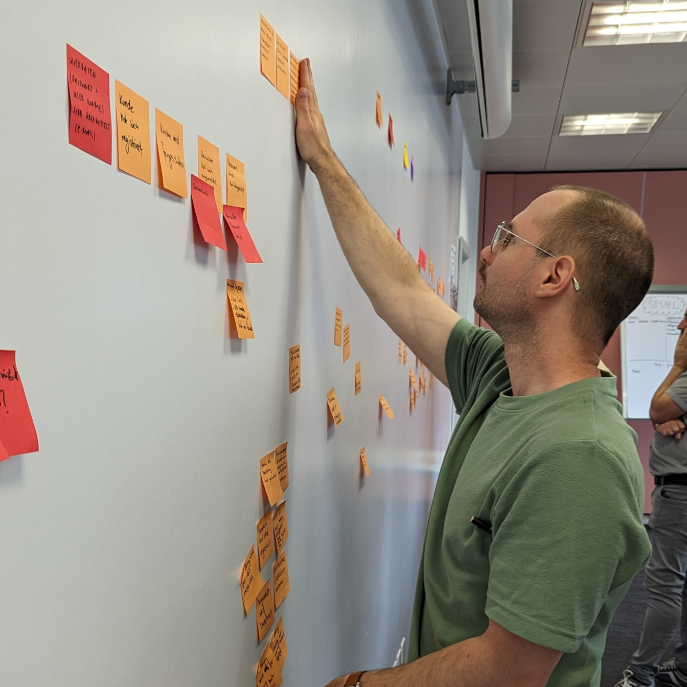Ein Mann klebt ein Post-it an eine Wand mit vielen weiteren Post-its