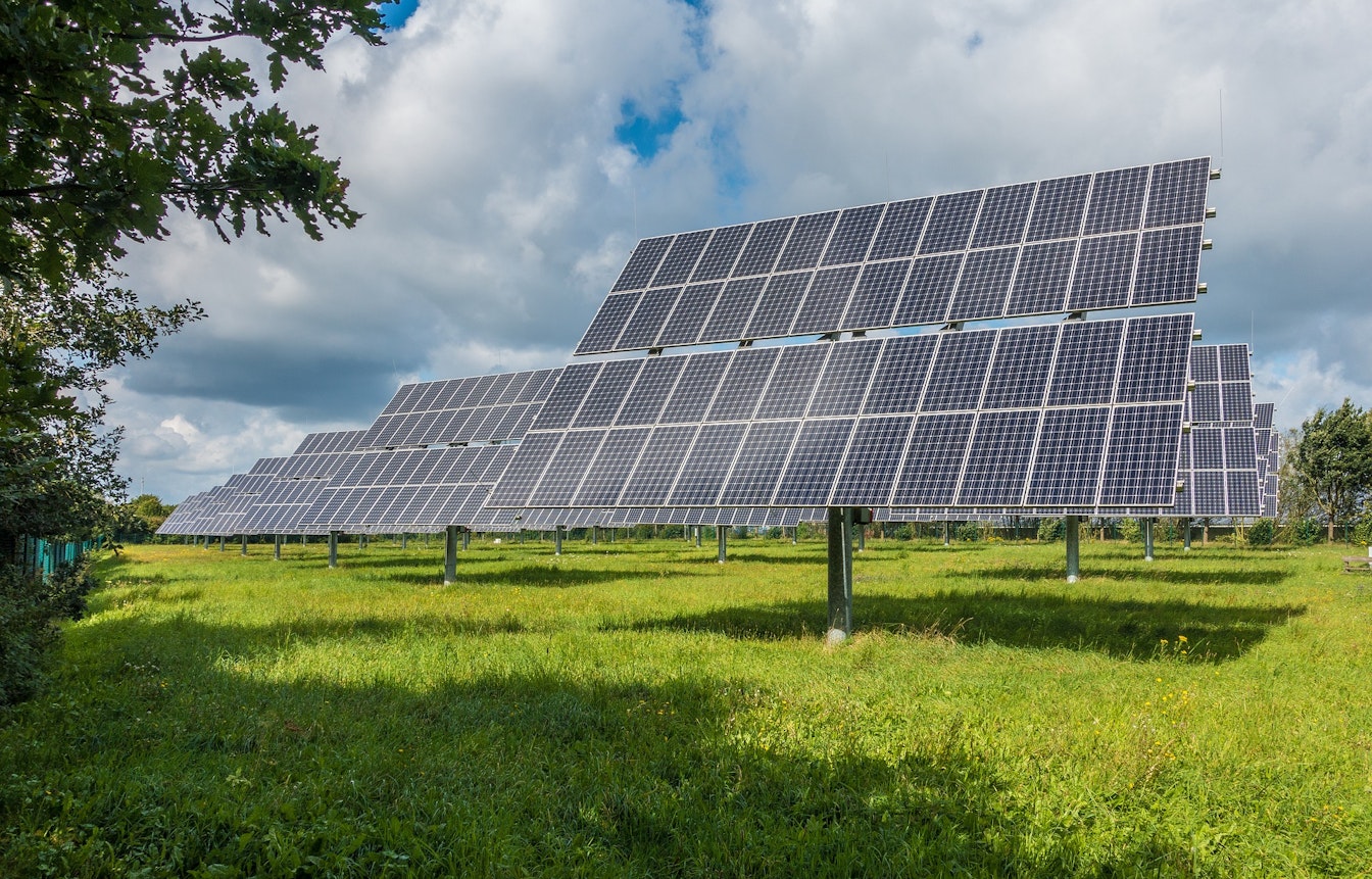 Reihen von Solarmodulen sind auf einer Wiese unter einem teilweise bewölkten Himmel installiert.