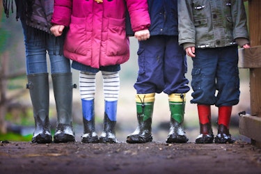 Eine Gruppe Kinder steht in einer Reihe. Sie tragen bunte Gummistiefel mit Schlamm darauf. Nur ihre Beine und Stiefel sind zu sehen.
