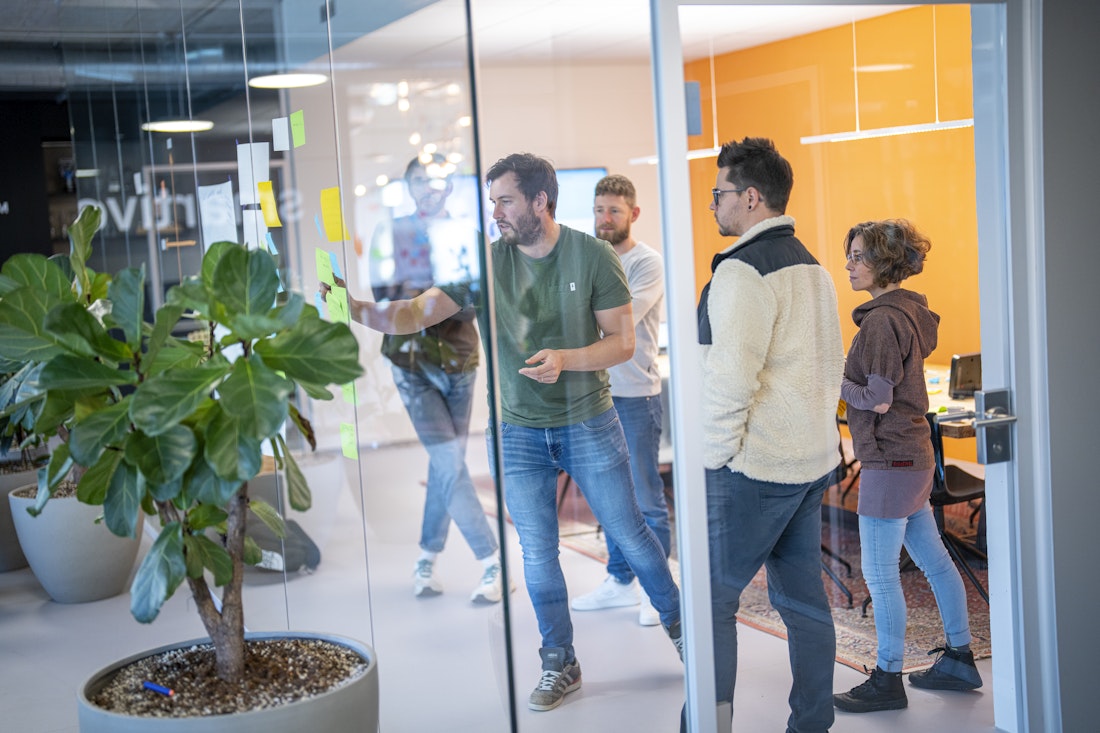 Vier Personen in einem Sitzungszimmer mit Glaswänden kleben Post-Its an die Wand während einem Workshop.