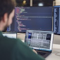 Eine Person arbeitet an einem Schreibtisch mit mehreren Monitoren, auf denen Code und Daten angezeigt werden.