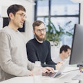 Zwei Personen arbeiten gemeinsam an einem Computerbildschirm in einem modernen Büro.