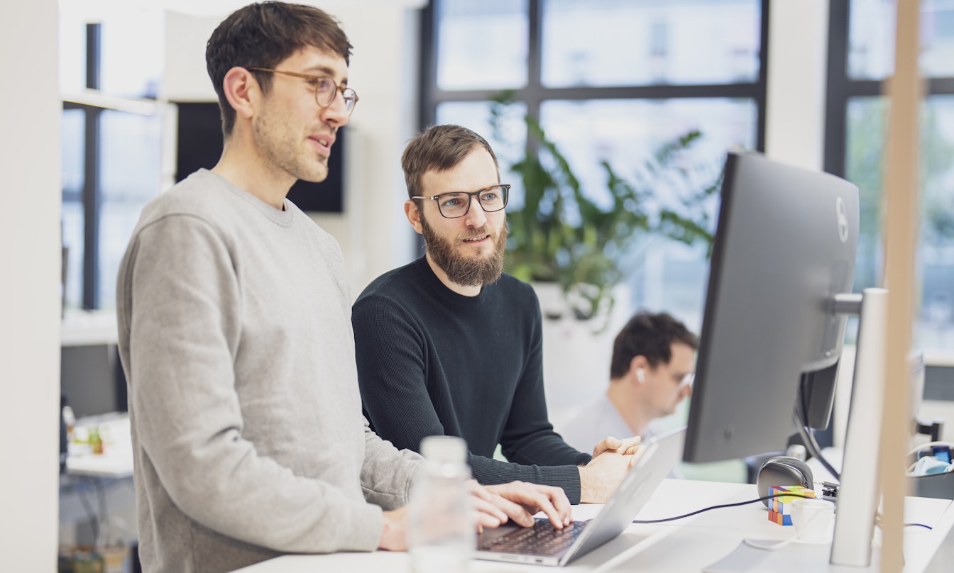 Zwei Personen arbeiten gemeinsam an einem Computerbildschirm in einem modernen Büro.