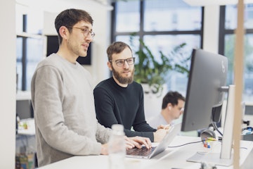 Zwei Personen arbeiten gemeinsam an einem Computerbildschirm in einem modernen Büro.