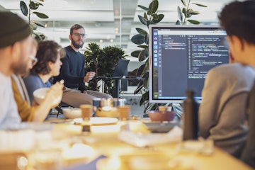 Mitarbeiter von smartive am Mittagstisch, die einem anderen Mitarbeiter bei einem Vortrag zuhören.