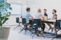 Vier Personen sitzen in einem Konferenzraum mit Glaswänden um einen Konferenztisch herum. Im Hintergrund zeigt ein grosser Bildschirm Informationen an.