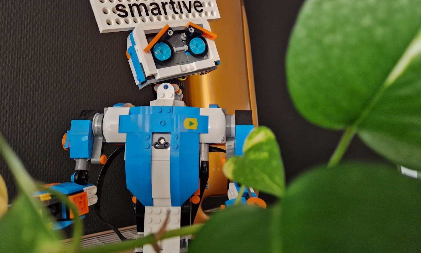 Lego-Roboter mit 'smartive'-Schild im Hintergrund, umgeben von grünen Pflanzen.