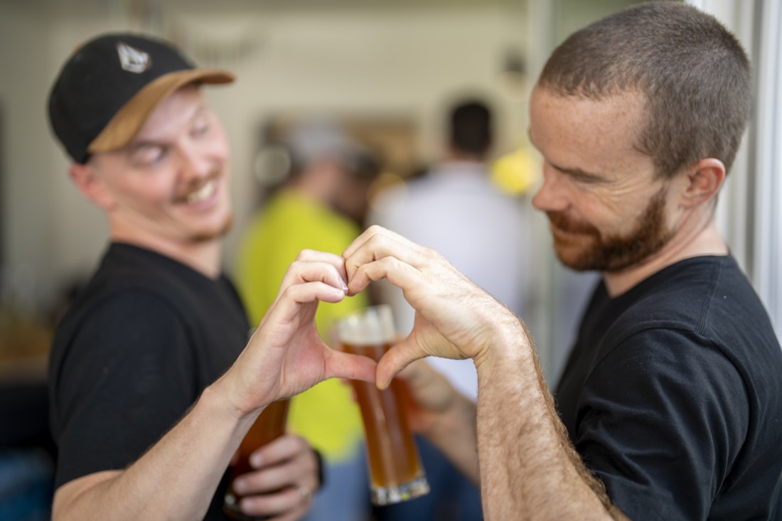 Zwei Männer formen mit ihren Händen ein Herz und trinken Bier.