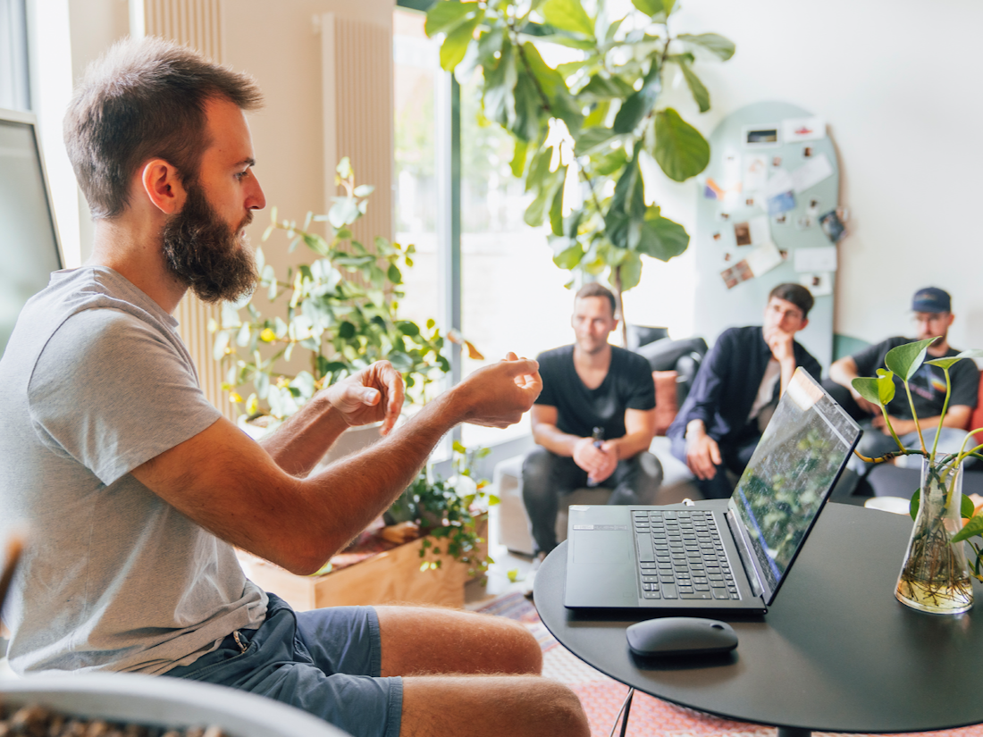 Ein Mann präsentiert vor einer kleinen Gruppe mit Laptop und Pflanzen im Hintergrund.