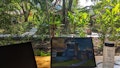 Laptops und eine Wasserflasche auf einem Holztisch mit einem üppigen Garten im Hintergrund.