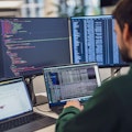 Eine Person arbeitet an einem Schreibtisch mit mehreren Bildschirmen, auf denen Code und Daten angezeigt werden.
(Hinweis: Der von Ihnen bereitgestellte Text enthält keine „ß“-Zeichen, der Inhalt bleibt also unverändert.).