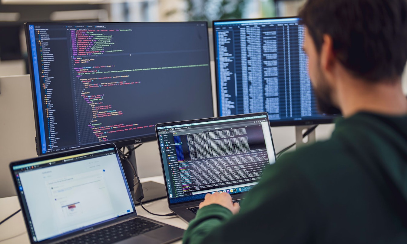 Eine Person arbeitet an einem Schreibtisch mit mehreren Bildschirmen, auf denen Code und Daten angezeigt werden.
(Hinweis: Der von Ihnen bereitgestellte Text enthält keine „ß“-Zeichen, der Inhalt bleibt also unverändert.).