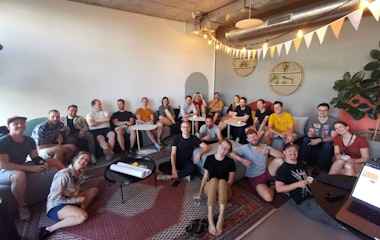 Eine Gruppe von Menschen sitzt auf Sofas und dem Boden in einem modernen, gemütlichen Raum mit Teppichen und Pflanzen.