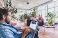 Drei Personen arbeiten an Laptops in einem hellen, modernen Büroraum mit großen Fenstern und viel Grün.