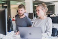 Ein Mann und eine Frau arbeiten gemeinsam an einem Schreibtisch mit Computern in einer modernen Büroumgebung.