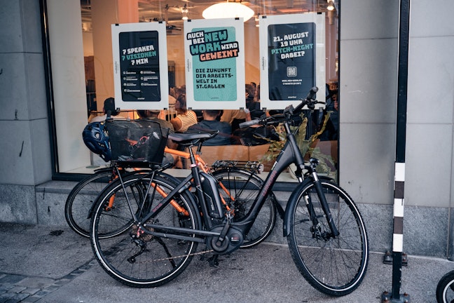 Zwei Fahrräder, die auf einem Bürgersteig vor dem Fenster eines Restaurants mit Plakaten geparkt sind.