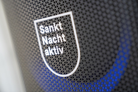 Nahaufnahme eines schildförmigen Schildes mit der Aufschrift "Sankt Nacht aktiv" auf einer gemusterten schwarzen Fläche mit blaüm Lichtakzent.