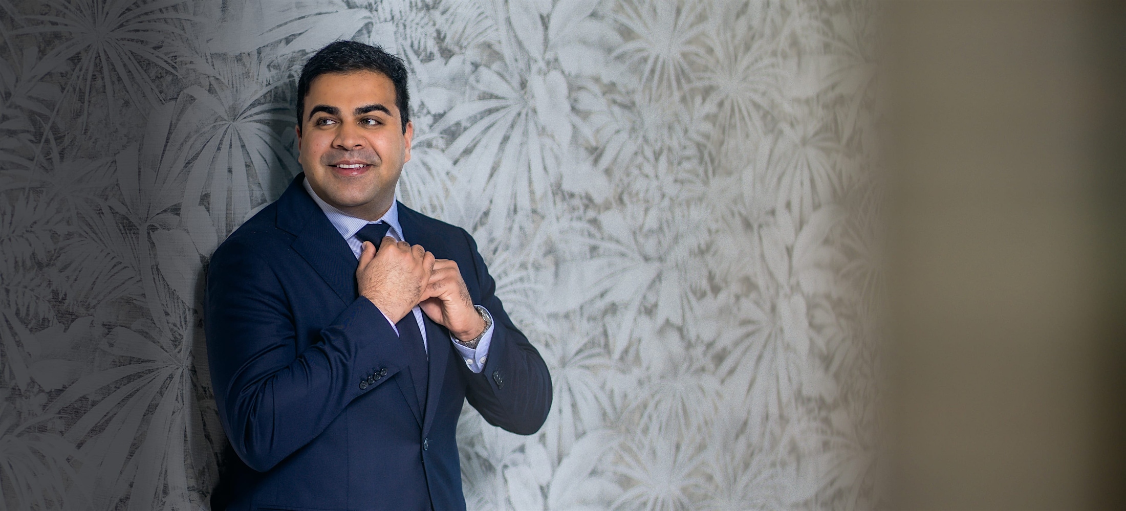 Dr. Chopra in a blue suit in front of a patterned wall
