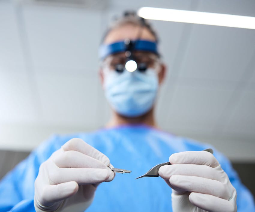 Dr. Guy in surgical uniform holding 2 tools