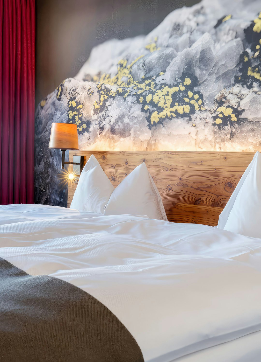 Sicht auf Doppelbett, darüber Foto mit Felsen, links roter Vorhang